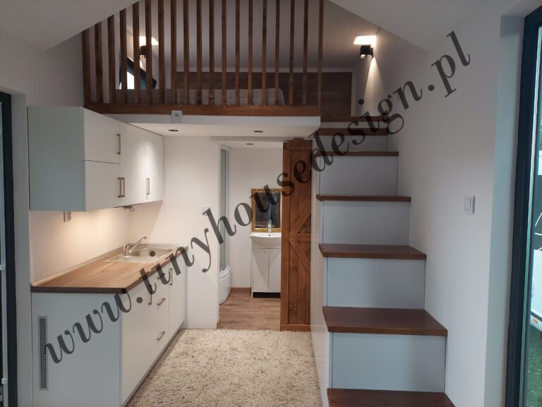 Aneks kuchenny, wejście do łazienki i schodki na antresolę w domku Tiny House Design w odcieniu bieli i drewna