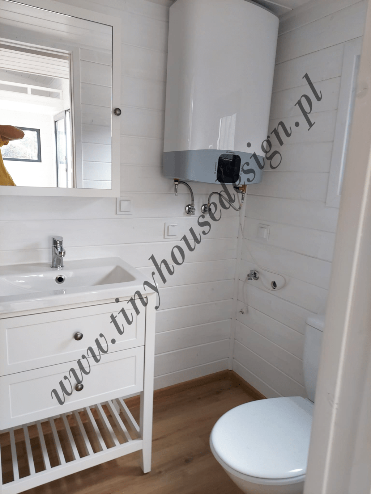 Łazienka w domku Tiny House Design - widok na umywalkę z szafką, lustro, boiler grzewczy i toaletę.